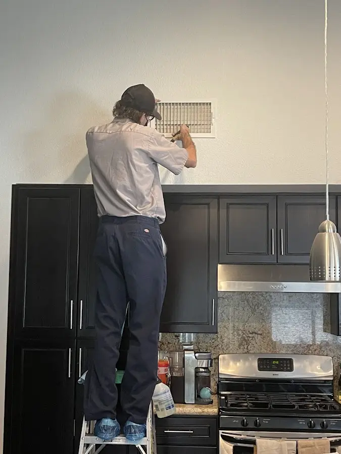 Technician inspecting an air vent during HVAC service in Seven Oaks